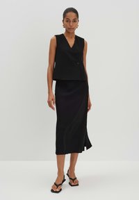 Schwarzes ärmelloses Top mit V-Ausschnitt und einem Knopfverschluss, kombiniert mit einem schwarzen Midiskirt aus Satin mit seitlichem Schlitz und minimalistischem Design.