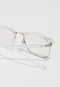 Clear, rectangular eyeglasses with metal accents. Lightweight transparent frames and straight temple arms. Lenses are slightly tinted.