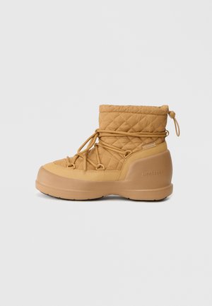 Botte étanche matelassée, de couleur beige, avec un bout rond, un laçage élastique et une semelle en caoutchouc texturé. Comprend un dessus matelassé et un logo sur le côté.