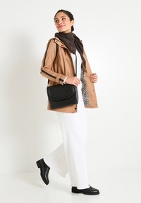 Femme portant un imperméable beige avec une doublure en imprimé léopard, une écharpe marron, un pantalon blanc et des bottes noires, portant un sac bandoulière noir, marchant avec confiance.