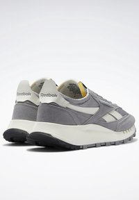 Paire de baskets Reebok grises et blanches avec semelles texturées, tige en suède et mesh, et languette de talon marquée, vue de l'arrière.