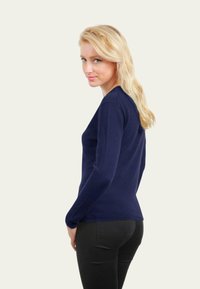 Haut à manches longues marine avec une silhouette ajustée, un col rond et des poignets côtelés. Texture lisse, associé à un pantalon ajusté noir.