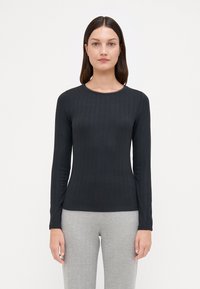 Svart langermet ribbestrikket topp med rund halslinning som har subtile perledetaljer. Glatt tekstur, tettsittende silhuett, brukt med lysegrå bukser.