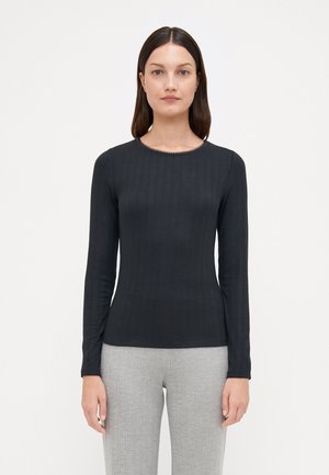 Maglietta nera a maniche lunghe a costine con scollatura rotonda e dettagli di perline sottili. Tessuto morbido, silhouette aderente, indossata con pantaloni grigi chiari.