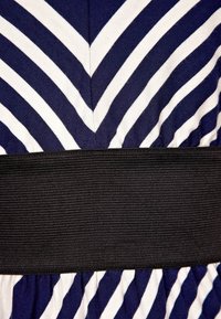 Laudot ja valkoiset vinoraidat kangasta, jossa on leveä teksturoitu musta vyö, joka korostaa vyötäröaluetta.