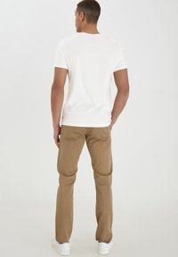 Hvit bomulls t-skjorte med korte ermer, i kombinasjon med lysebrune bomullsbukser og hvite sneakers, sett fra bak.