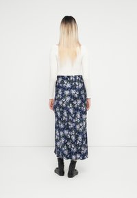 Blommig maxikjol med mörkblå bakgrund, lila blommor och gröna detaljer; har en mjuk tygkvalitet och elastisk midja.