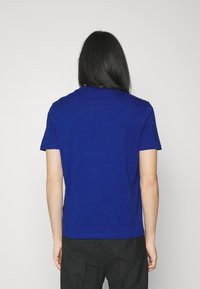 Kratké rukávy, modré bavlněné tričko s kulatým výstřihem a hladkou texturou, zobrazené zezadu na jednoduchém bílém pozadí.