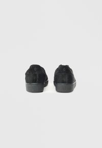 Mustad mustad, millel on tekstuuriga materjal, ümmargune nina ja pehme viimistlus. Väljaspoolne tald on tekstuuriga, minimaalsete õmbluste ja logodetailiga.