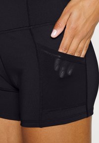 Černé sportovní šortky s bezešvým provedením a síťovanou kapsou. Materiál je pružný a hladký, s viditelnými detaily švů.