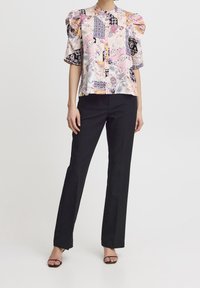Blouse à motifs floraux avec manches bouffantes, principalement en pastels et noir, associée à un pantalon noir ajusté. Tissu lisse et coupe décontractée.