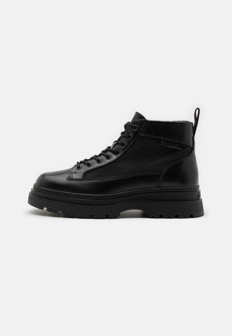 Schwarze Knöchelstiefel aus Leder und Mesh, mit runder Spitze, stabiler Sohle und einem Ziehlasche hinten. Strukturiertes Oberflächen-Design.