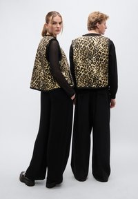 Puha anyagú ujjatlan mellény leopárdmintával, fekete hosszú ujjú felsőkkel és bőszárú fekete nadrággal párosítva. Lapos cipőkkel egészül ki az összhatás.