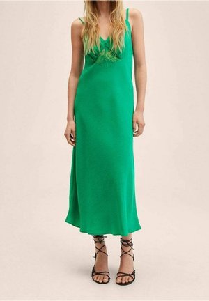 Robe maxi verte sans manches avec un corsage ajusté et un ourlet évasé. Caractérisée par un col texturé et fabriquée en tissu léger. Sandales noires à lacets.