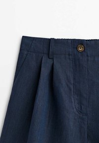 Pantalons en lin bleu marine avec des plis, une taille avec un bouton marron et des poches latérales. Texture lisse avec une coupe structurée.