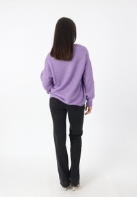 Übergroßer lila Pullover aus weichem Strickstoff, kombiniert mit schwarzen, eng anliegenden Jeans. Die Rückansicht zeigt fallende Schultern und gerippte Bündchen.