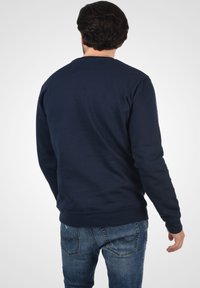 Mørkeblå sweatshirt med lange ærmer, ribbede manchetter og rund halsudskæring. Fremstillet af blødt stof, med en glat tekstur og minimal detaljering.