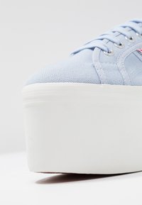 Světle modré plátěné tenisky s texturovaným svrškem, bílou platformou a stříbrnými očka. Mají kulatou špičku a šněrování.