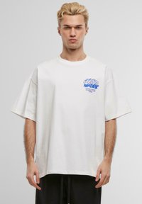 Hvit oversized bomull t-skjorte med blå grafikktrykk på venstre bryst, rund hals og korte ermer. Enkel og uformell design.