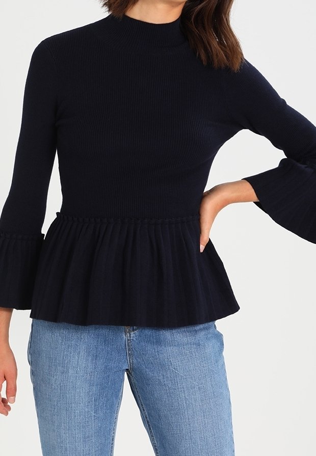 Mörkblå ribbad trikå peplum-top med hög krage, utsvängda långärmar och volangdetalj vid midjan; kombinerad med ljusblå jeans.