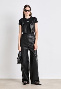 Μαύρο δερμάτινο κον τό γιλέκο πάνω από ένα μαύρο t-shirt, συνδυασμένο με ψηλόμεσα μαύρα δερμάτινα παντελόνια σε φαρδιά γραμμή. Τα αξεσουάρ περιλαμβάνουν μαύρα γυαλιά ηλίου και μια τσάντα ώμου.