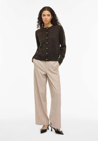 Brun strikket cardigan med rund hals, knapper foran og lange ermer, kombinert med lysebeige vidbukser og svarte høye hæler.