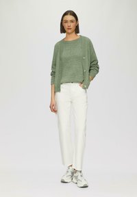 Cardigan en tricot vert clair avec des boutons, associé à un haut en tricot assorti et un pantalon blanc à jambe droite, complété par des baskets grises.