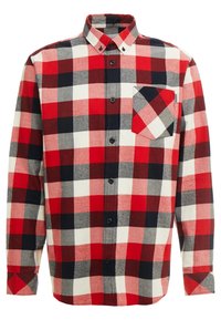 Camisa de franela a cuadros en rojo, negro y blanco con cuello abotonado, mangas largas y un bolsillo en el pecho con el mismo patrón.