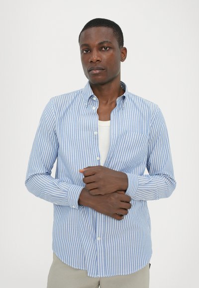 Camisa de botones a rayas azul y blanca, hecha de algodón, con cuello y un solo bolsillo en el pecho, de pie frente a un fondo liso.