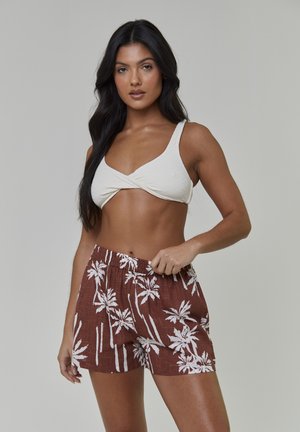 Haut de bikini en tricot crème avec larges bretelles et devant torsadé, associé à un short marron avec imprimé palmiers blancs et une taille élastique.