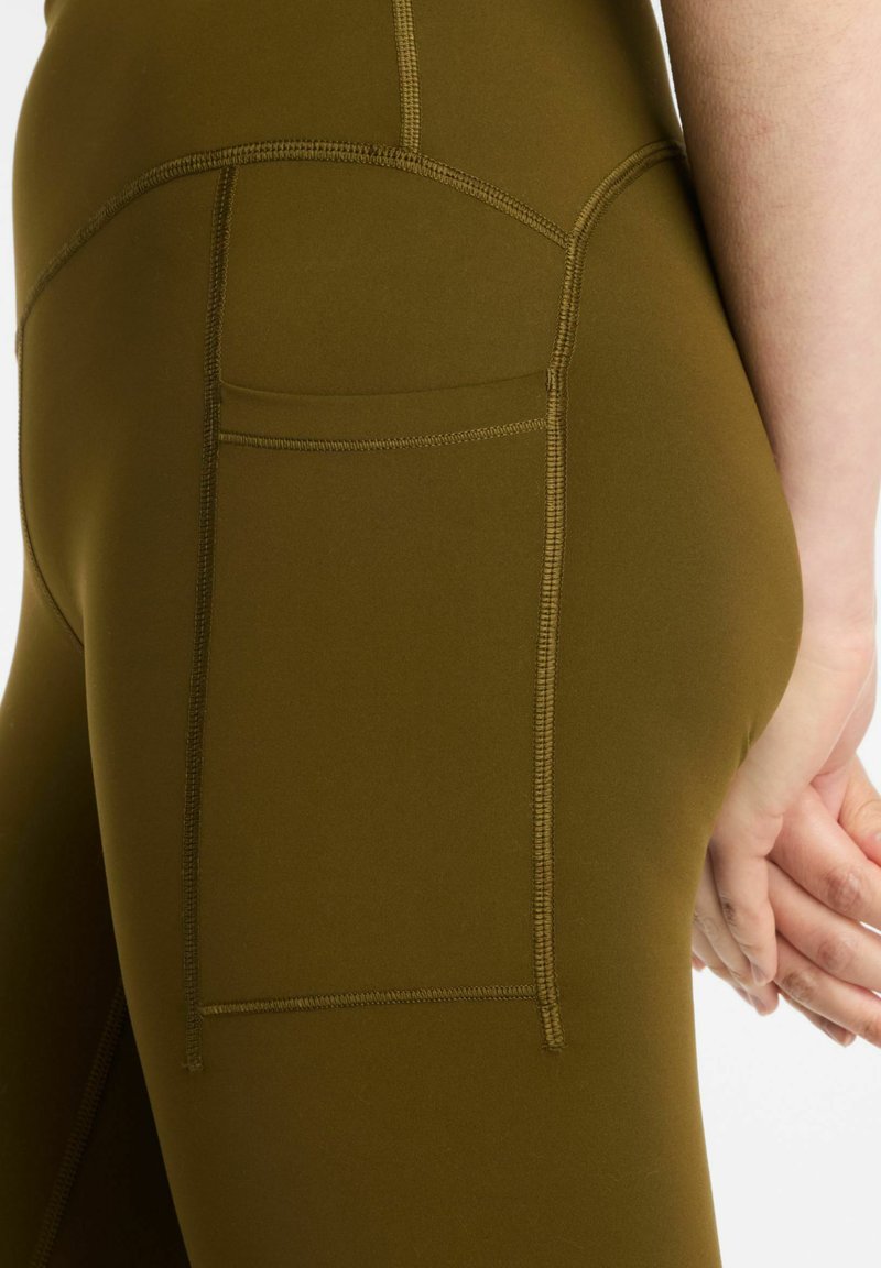 Olivgröna sportleggings med slät textur, utrustade med en sidoficka och kontrasterande sömmar längs sömmarna.