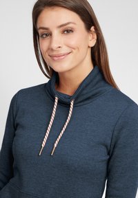 Sötétkék kapucnis pulóver puha anyagból, dorkorom nyakkal, állítható, réz végekkel ellátott zsinórokkal és bordázott részletekkel a nyak körül.