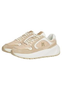 Sneaker beige chiaro realizzate in suede e tessuto con dettagli bianchi, dotate di suola spessa, allacciatura e logo sulla parte laterale.