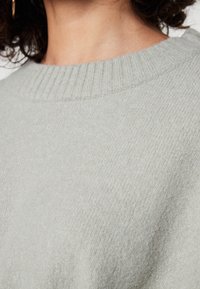 Maglione grigio chiaro lavorato a maglia con un collo a coste. Il tessuto appare morbido e strutturato, con un motivo sottile nella trama.