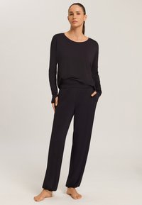 Černá souprava na domácí nošení, která obsahuje dlouhý rukáv s kulatým výstřihem a kalhoty s elastickým pasem a kapsami. Měkká, hladká tkanina.