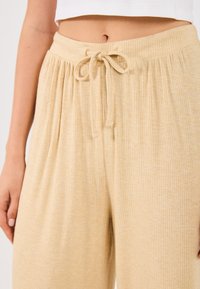 Ανοιχτό μπεζ ριγέ παντελόνι lounge με ελαστική ζώνη, που διαθέτει μαλακή υφή και χαλαρή εφαρμογή. Δεν υπάρχουν ορατές τσέπες ή διακοσμητικά.