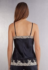 Svart satin cami med tunna axelband, prydd med krämfärgad spets längs den övre kanten och fållen, med en mjuk textur och en figurnära design.