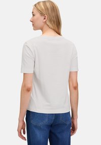 T-shirt gris clair à manches courtes avec un col rond, en tissu doux, vu de dos, associé à un jean en denim bleu.