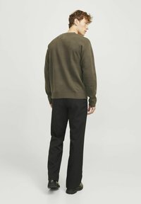 Olivgrüner Pullover mit rundem Ausschnitt und langen Ärmeln, kombiniert mit schwarzen Hosen. Glatte Textur; tailliert.