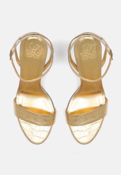 Guld sandaler med et elegant design, der har en glat, skinnende overdel og en tekstureret krokodillemønstret strop. Ankeldesign med flere stropper.