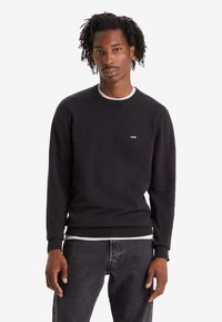 Sweatshirt noir à col rond en coton avec un col et un ourlet côtelés, arborant un petit logo Levi's blanc sur la poitrine. Associé à un jean foncé.