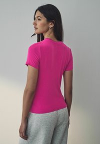 T-shirt aderente rosa a righe con maniche corte, scollatura rotonda e texture liscia, abbinato a pantaloni della tuta grigi chiari.