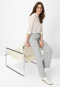 Lichte, knoopsluiting wit linnen overhemd, grijze linnen broek met elastische taille, witte sneakers, zittend op een moderne, gewatteerde stoel met een chroomframe.