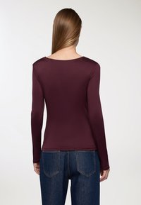 Top bordeaux a maniche lunghe in tessuto liscio con scollatura rotonda. Abbinato a jeans in denim blu a vita alta, con tasche e cuciture in vista.