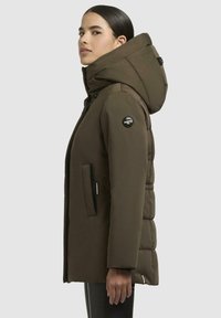 Braune gepolsterte Jacke mit großer Kapuze, seitlichen Taschen und einem runden Logo-Patch am Ärmel. Glatte Textur und mittellanges Design.