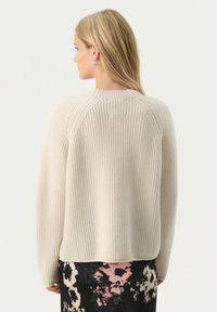 Beige ribstrikket sweater med rund halsudskæring og raglanærmer, der har en afslappet pasform og en kant, der bøjer let opad i bunden.