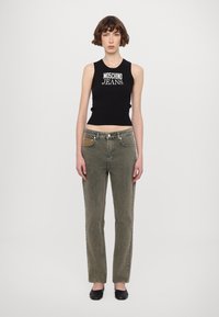 Juodas surištas rankovių marškinėliai su "Moschino Jeans" užrašu; alyvuosių žalios tiesios kojos džinsai su kontrastiniais kišenės bei šoninių detalių akcentais. Juodi butai.