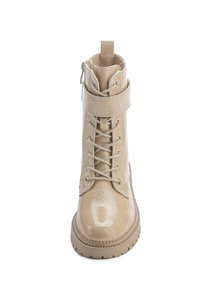 Bottine en cuir verni beige avec des lacets à l'avant, une sangle à la cheville, un bout arrondi et une semelle en caoutchouc texturé. Fermeture éclair sur le côté.