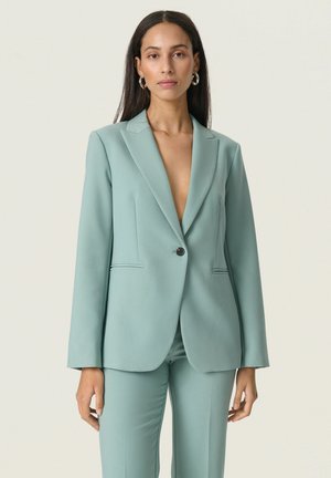 Hellgrüner taillierter Blazer mit Reverskragen, Ein-Knopf-Verschluss und zwei Fronttaschen. Glatte Textur, lange Ärmel.