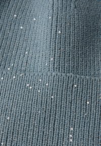 Tejido de punto en azul apagado, con textura de canalé vertical y lentejuelas brillantes distribuidas para un detalle adicional. Material suave y flexible.